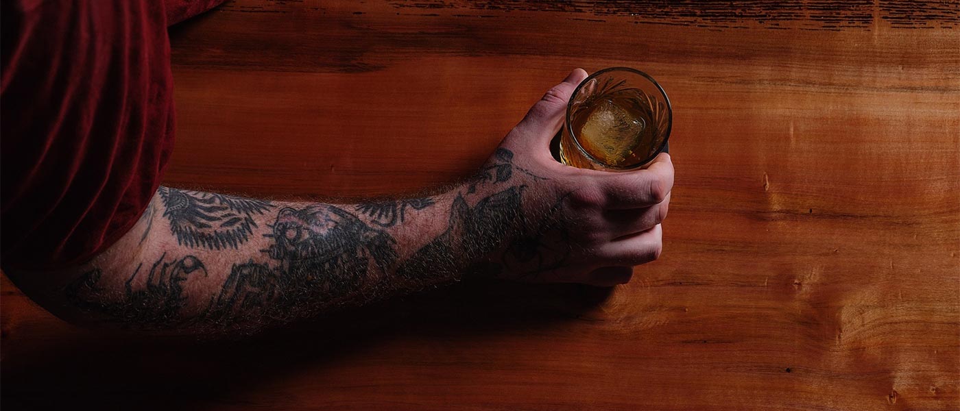 The tattooed arm of Joel Alderice, owner of Emerald City, at the beautiful wooden bar with a whisky.